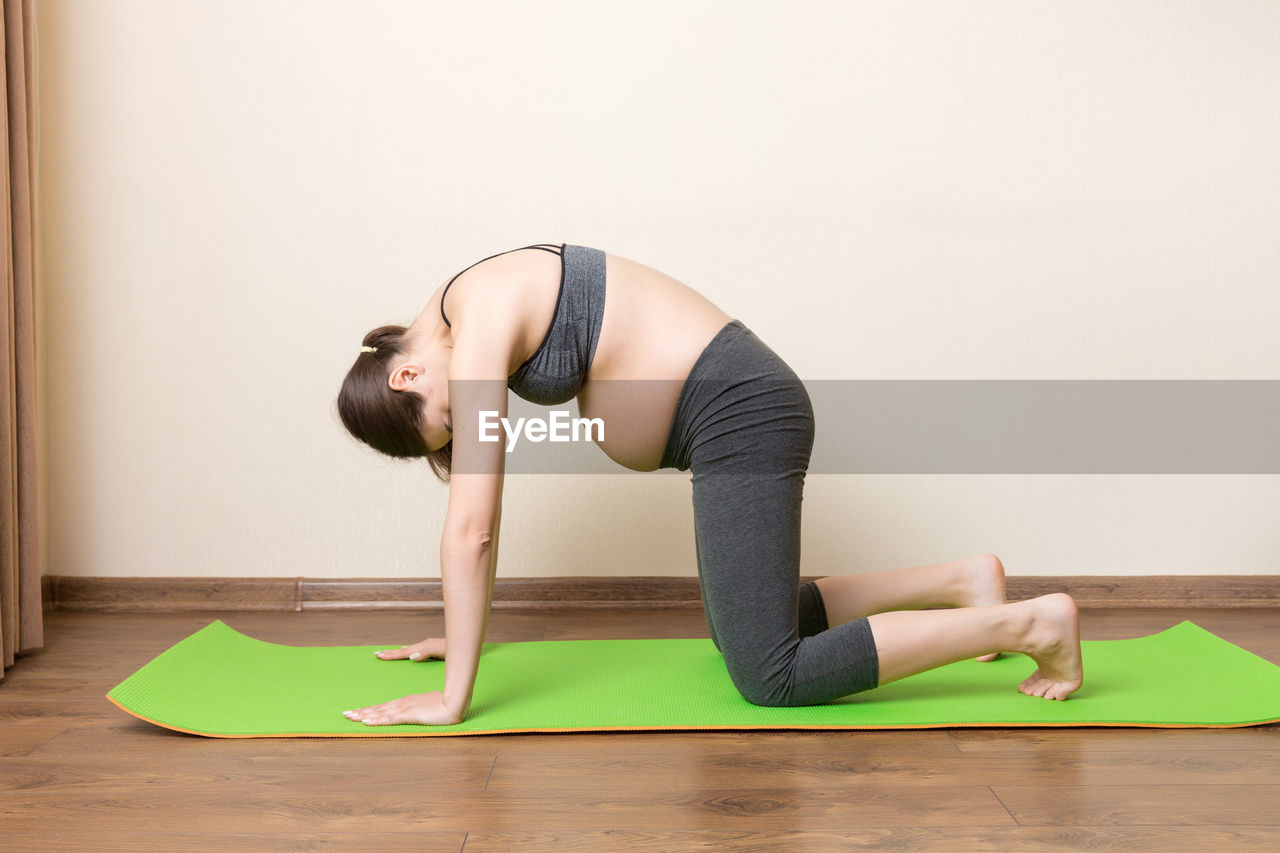 WOMAN WEARING HAT WHILE SITTING ON FLOOR AGAINST WALL