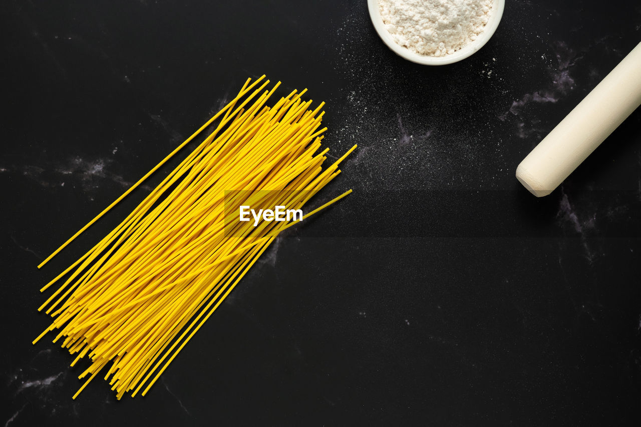 Concept of making spaghetti noodles.cup of flour.flour,rolling pin,noodles on dark background.