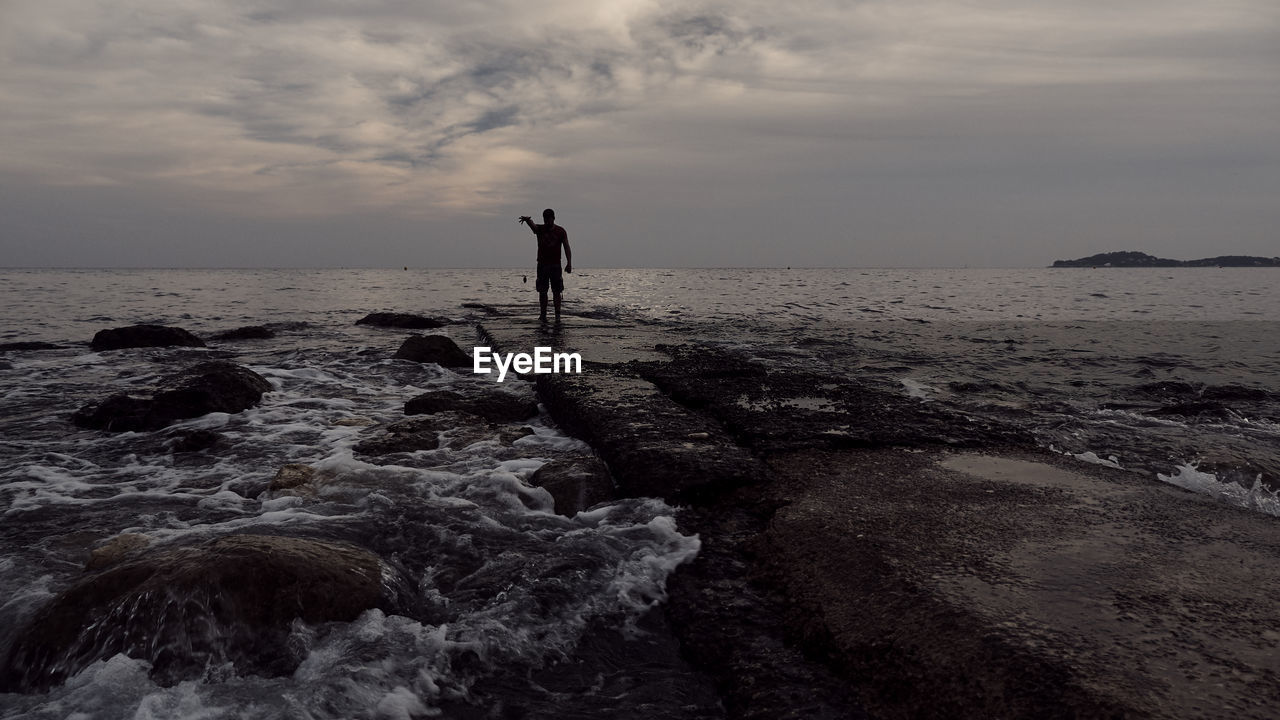 Man standing in sea against sky during sunset