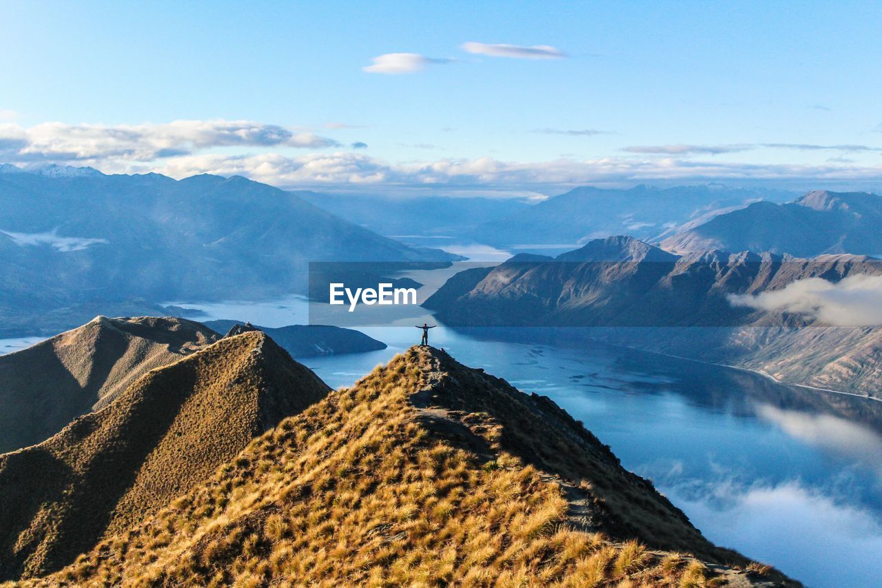 Scenic view of mountains and river with man standing against sky