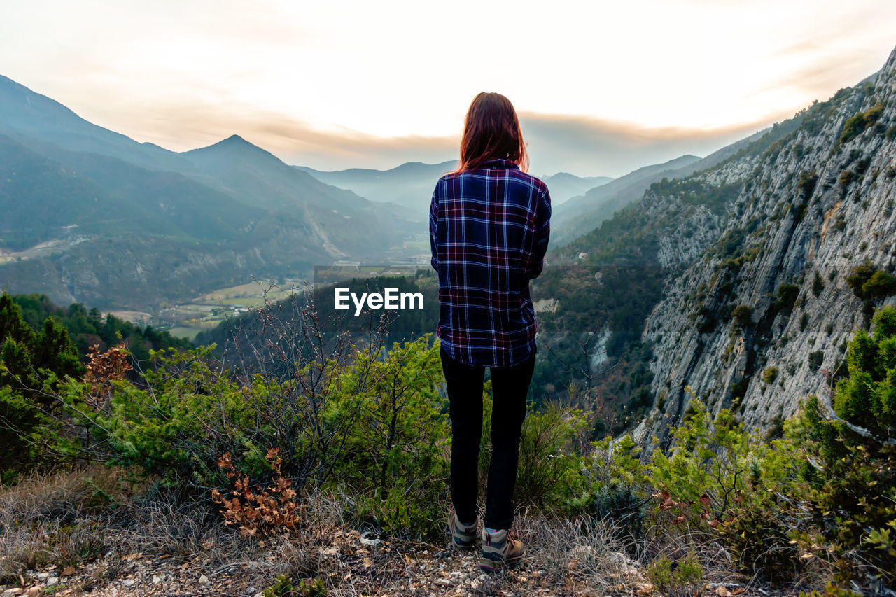 Rear view of woman standing on mountain against sky