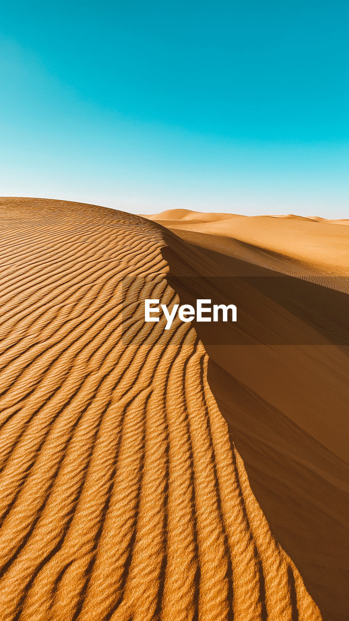 Sand dunes in desert against clear blue sky