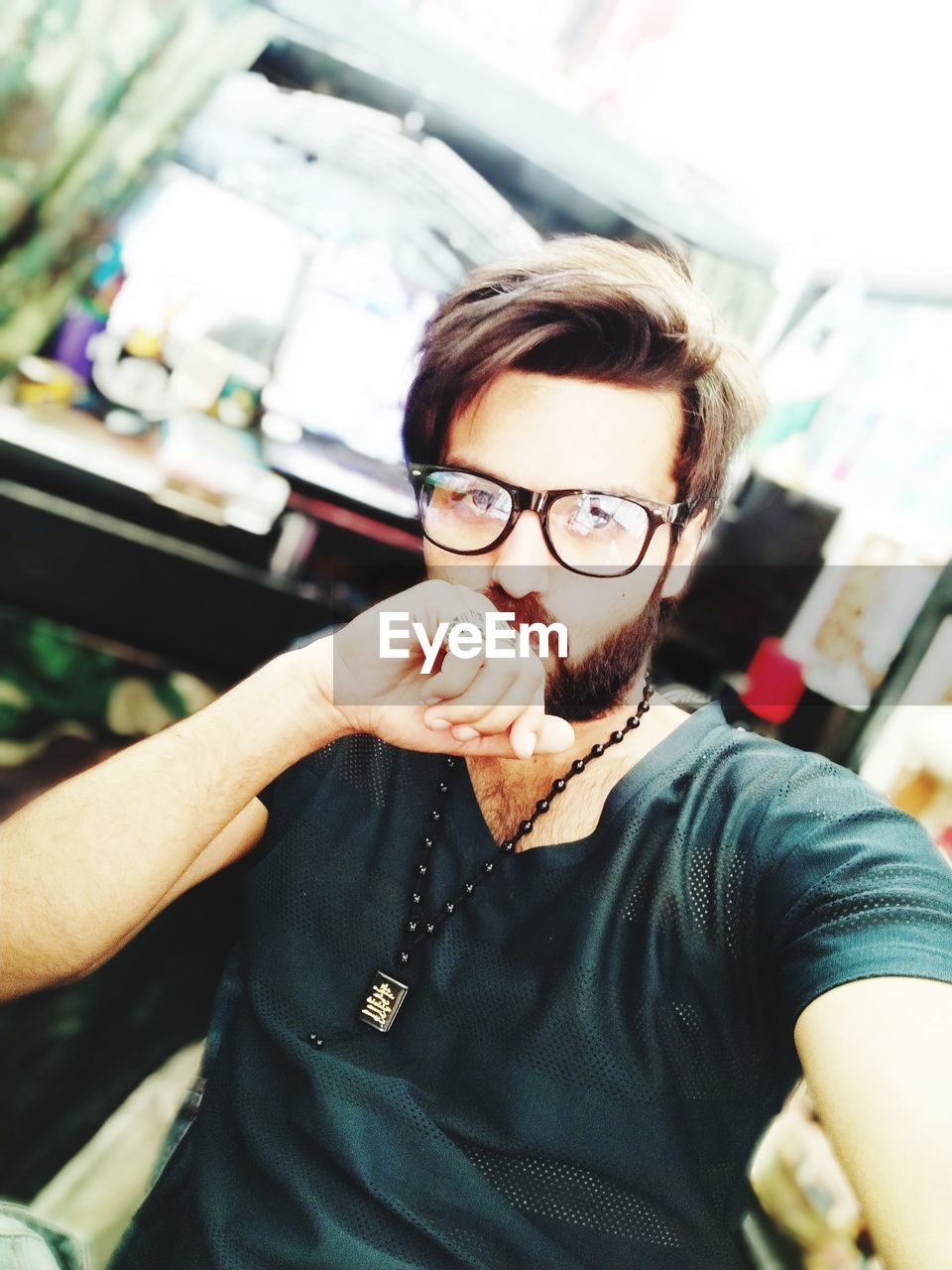 PORTRAIT OF YOUNG MAN STANDING BY EYEGLASSES