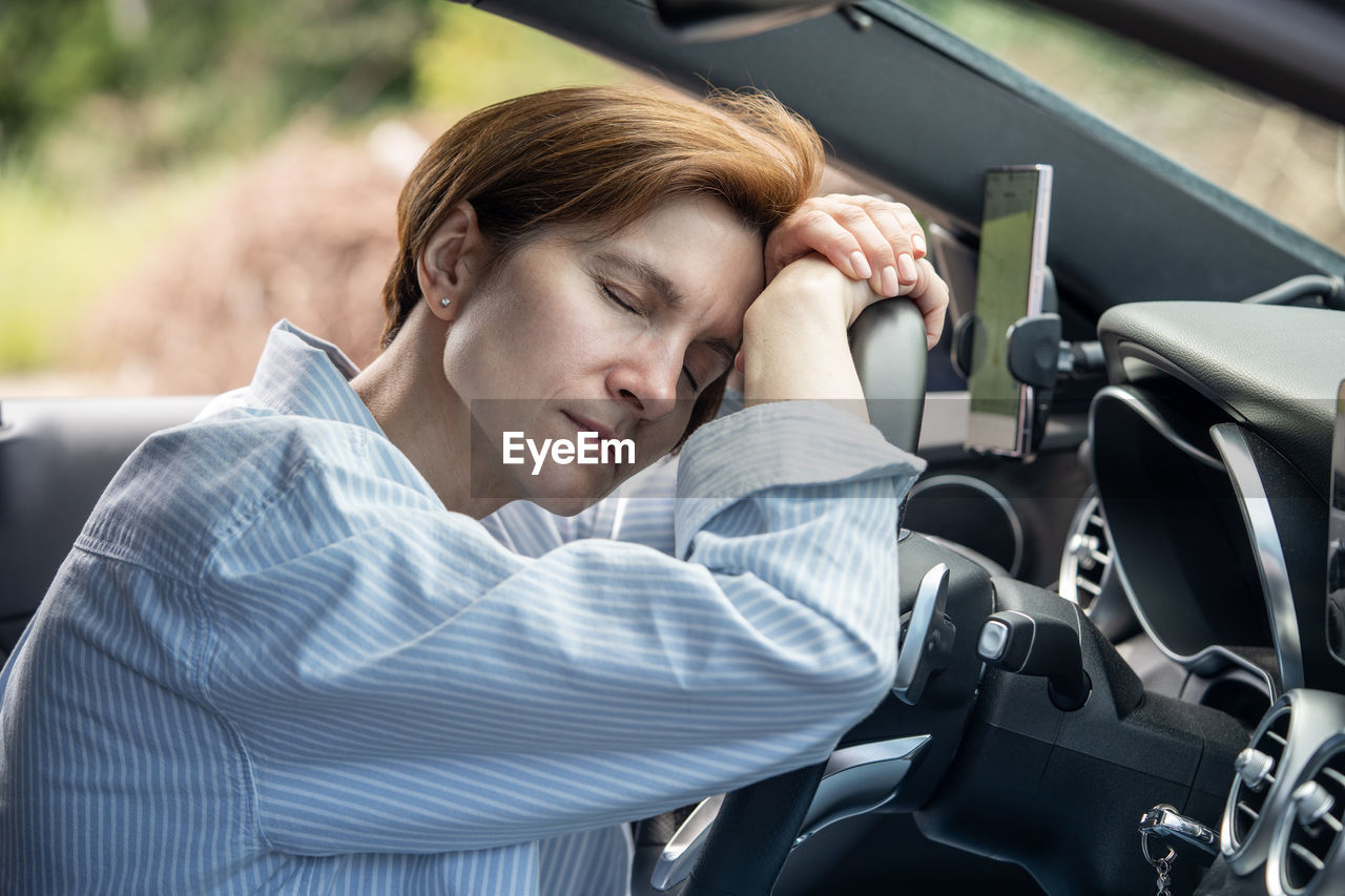 Middle aged tired woman sleeping on steering wheel exhausted from long driving in road trip.