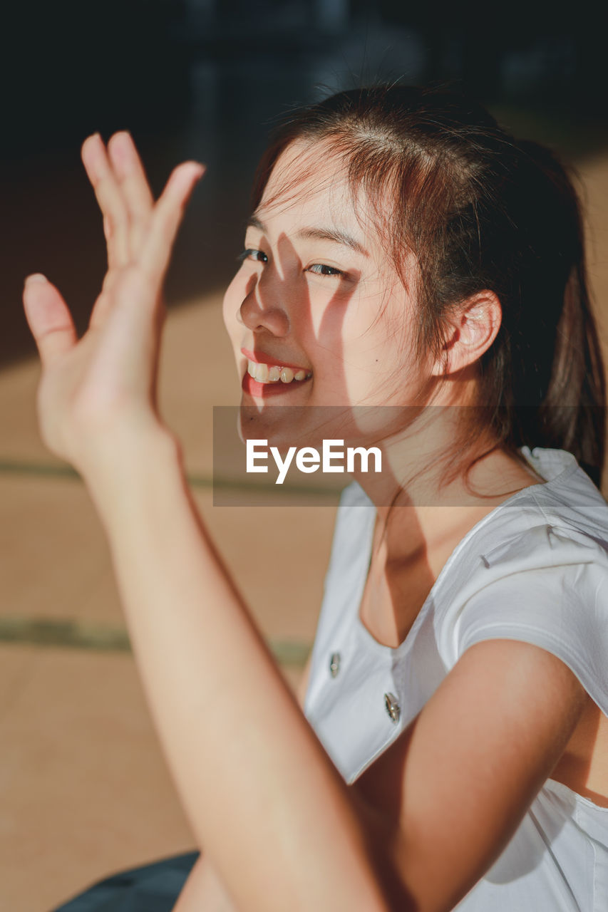 Portrait of smiling young woman shielding eyes while sitting on floor