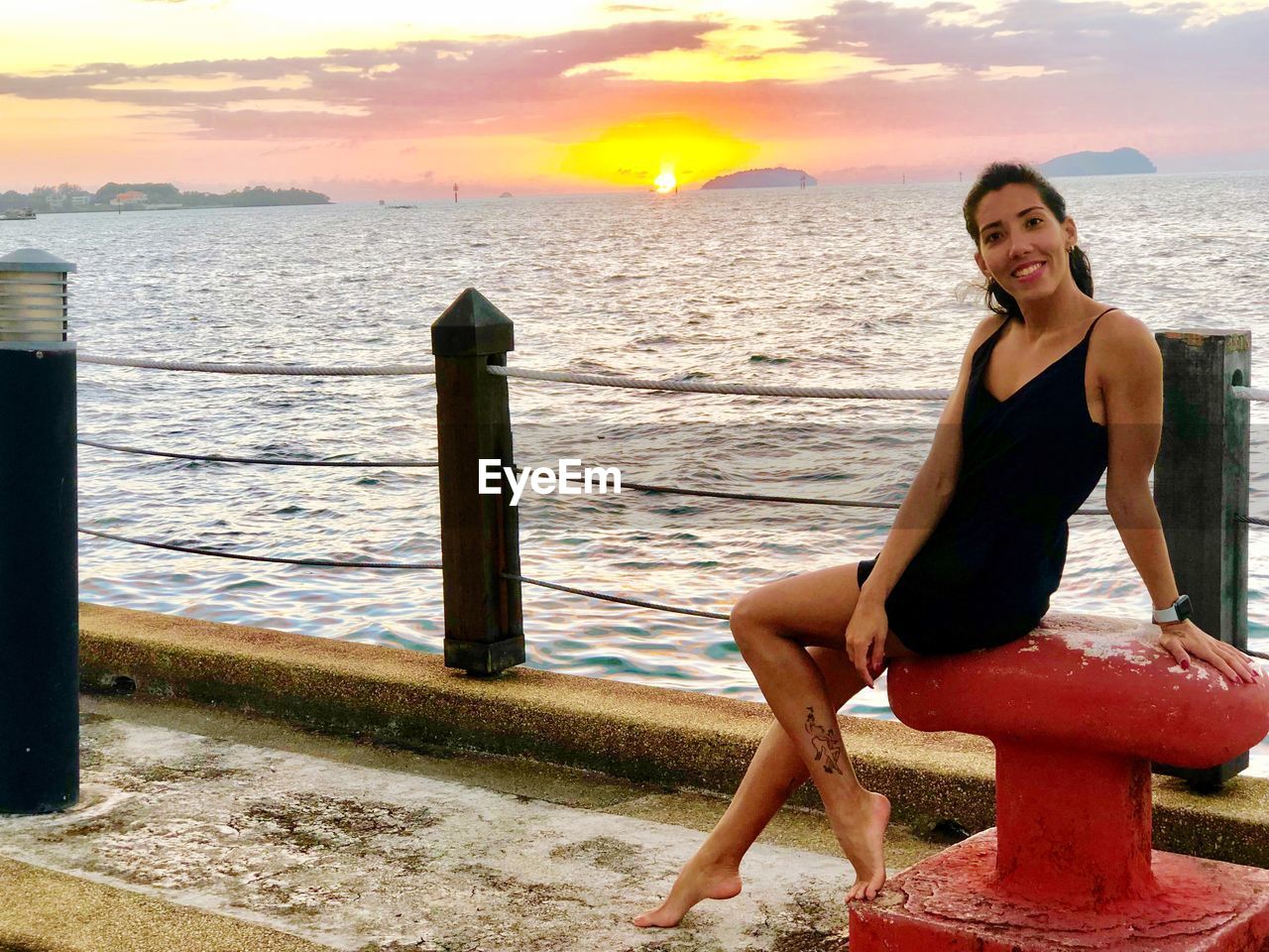 PORTRAIT OF SMILING YOUNG WOMAN SITTING BY SEA