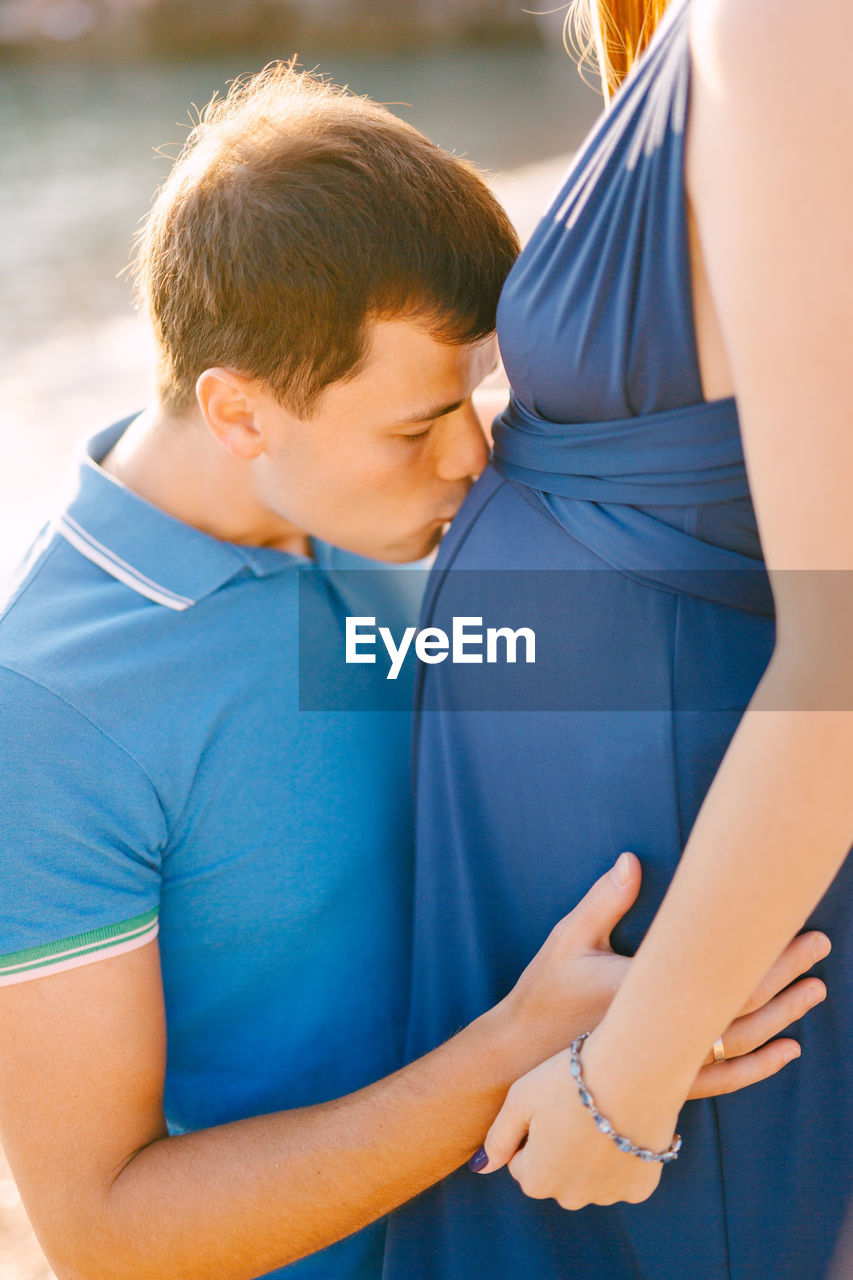 Man kissing woman stomach outdoors