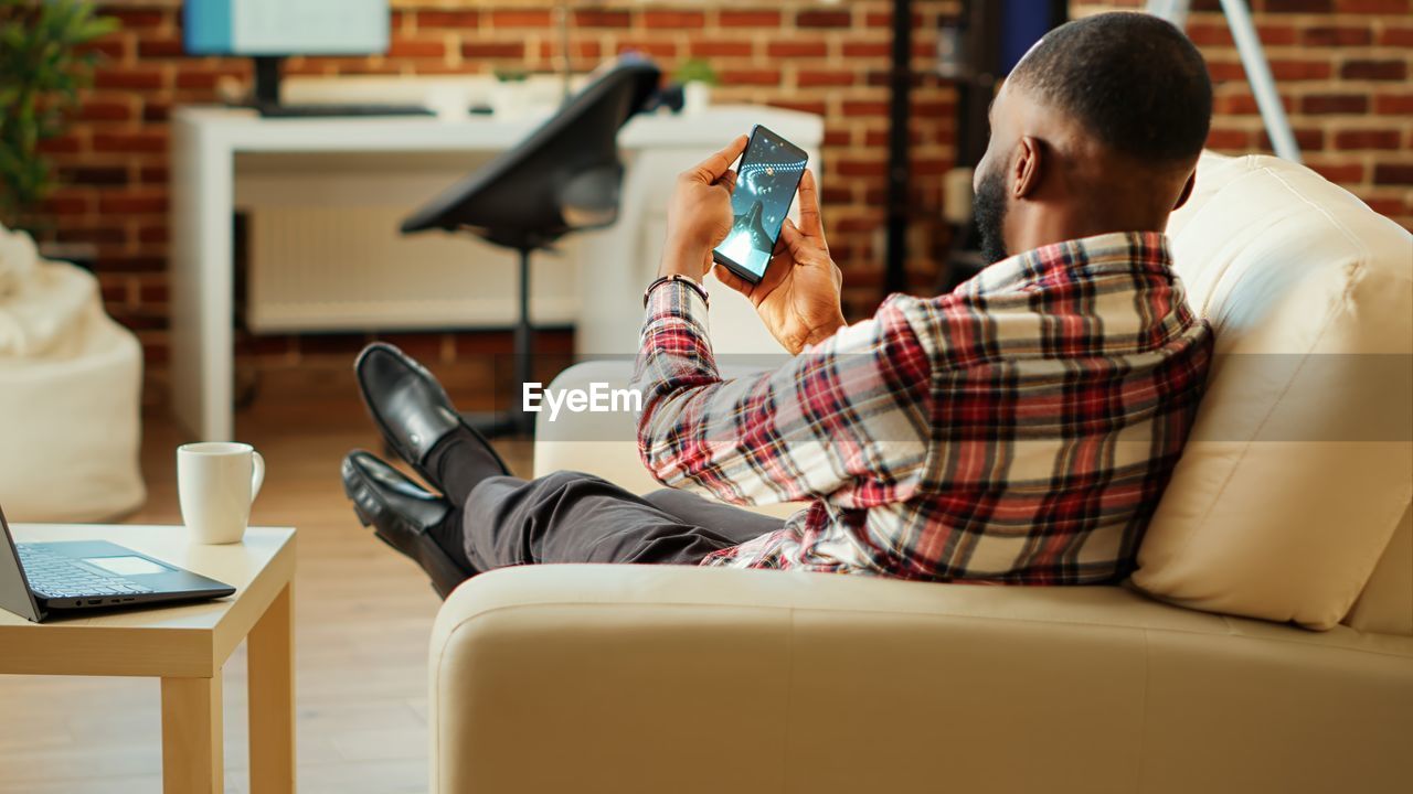 young woman using mobile phone while sitting on sofa at home
