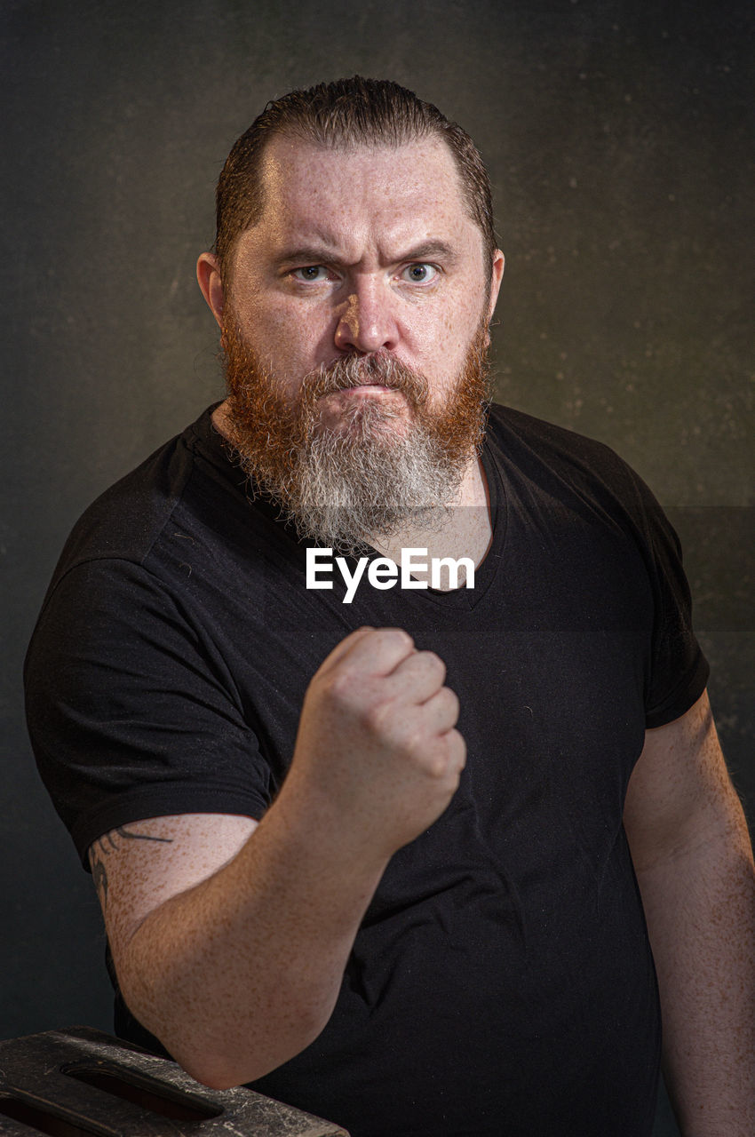 facial hair, adult, beard, one person, men, portrait, studio shot, person, human hair, looking at camera, mature adult, indoors, waist up, hairstyle, lifestyles, serious, black, casual clothing, emotion, front view, arm, anger, hand, facial expression, human face, black background