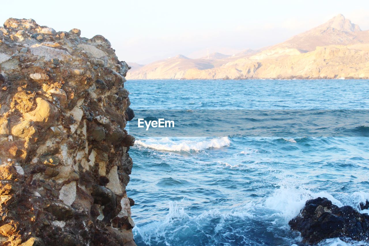 SCENIC VIEW OF ROCKS ON SEA AGAINST MOUNTAINS