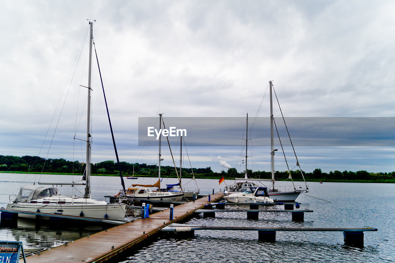 Sailboat moored by jetty at lake against cloudy sky