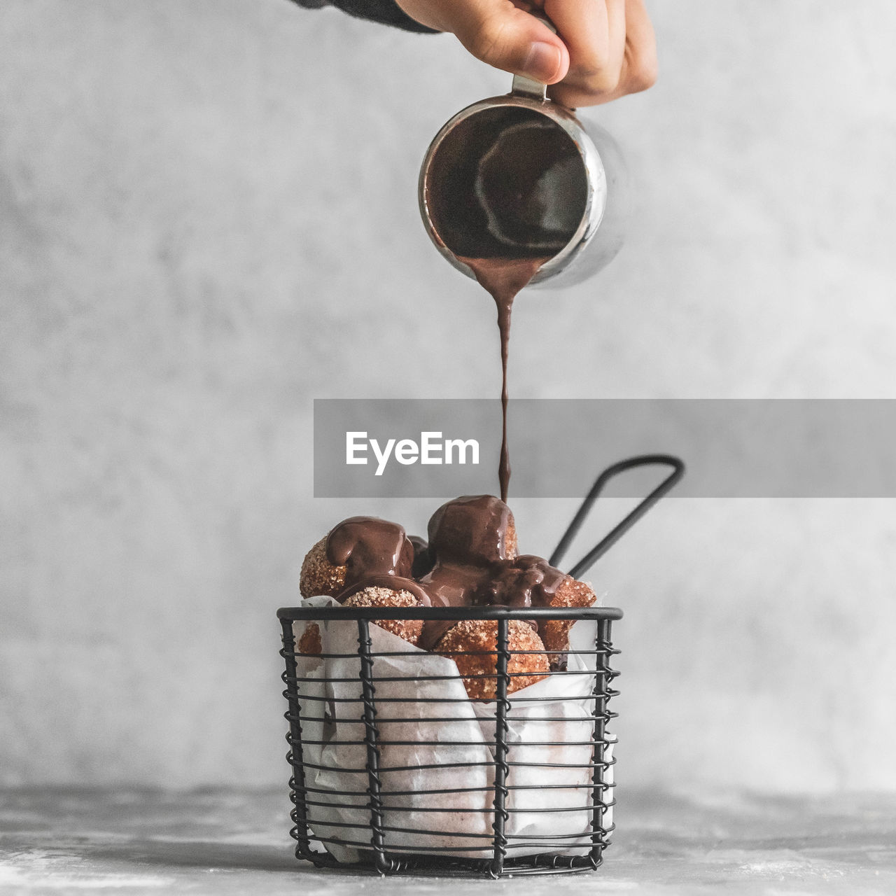 Close-up of hand pouring chocolate over donut holes churros on table against wall