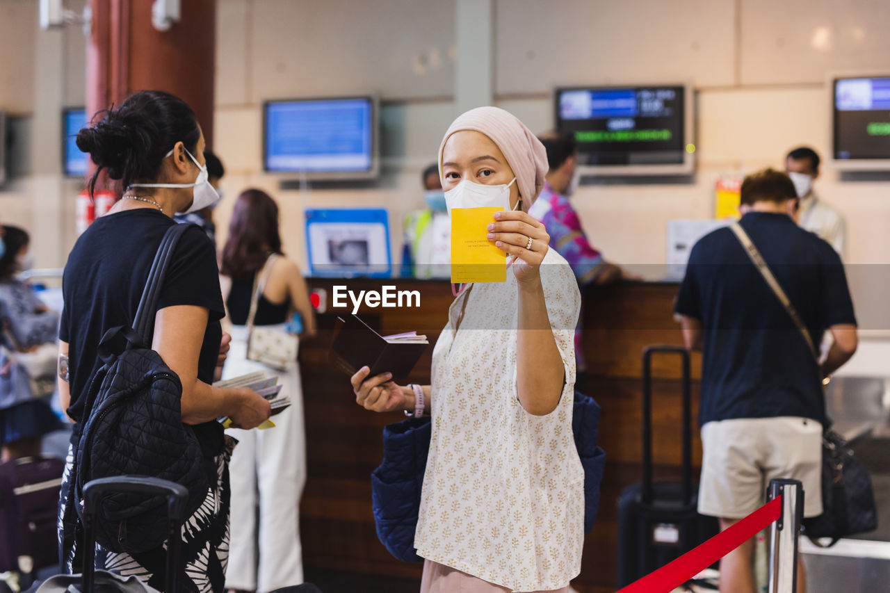 Asian woman in face mask check in at airport and showing her vaccination record