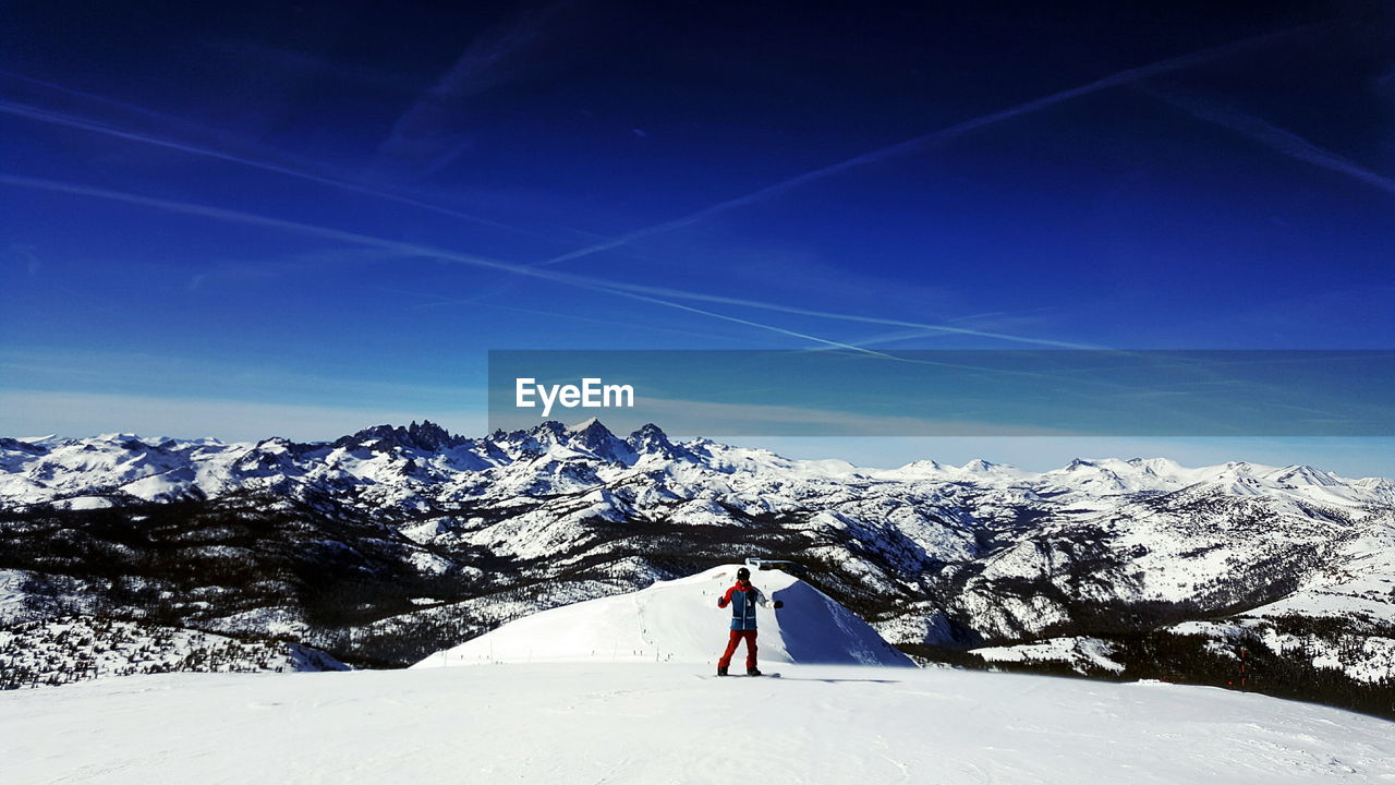 Man skiing on snowcapped mountain against blue sky