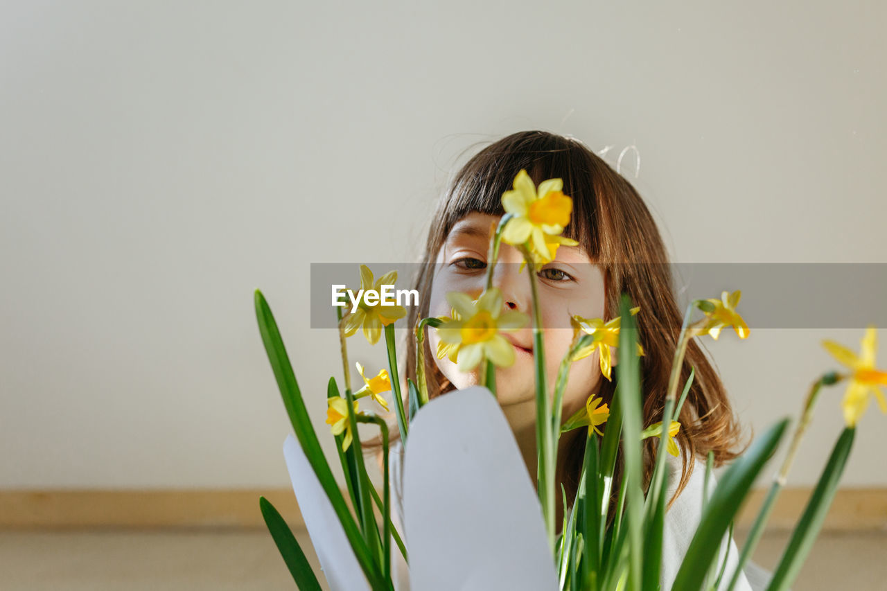 Portrait of little girl hiding behind yellow daffodil flowers