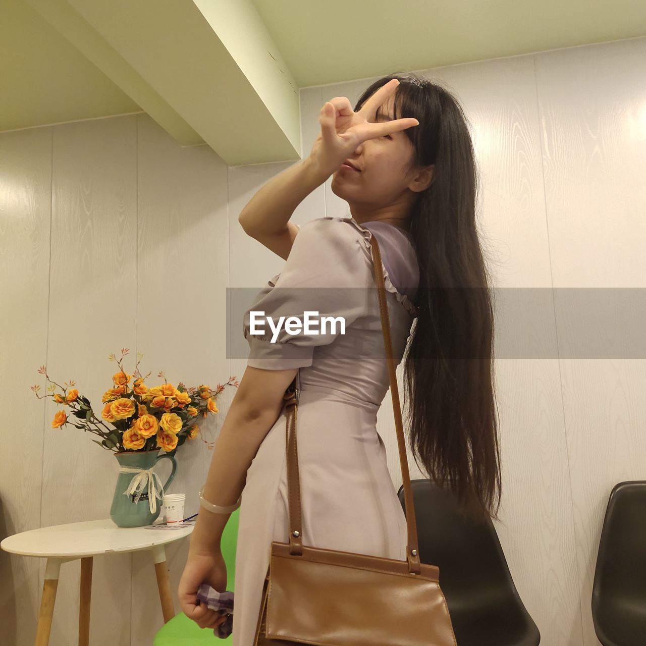 Young woman showing peace sign while standing at home