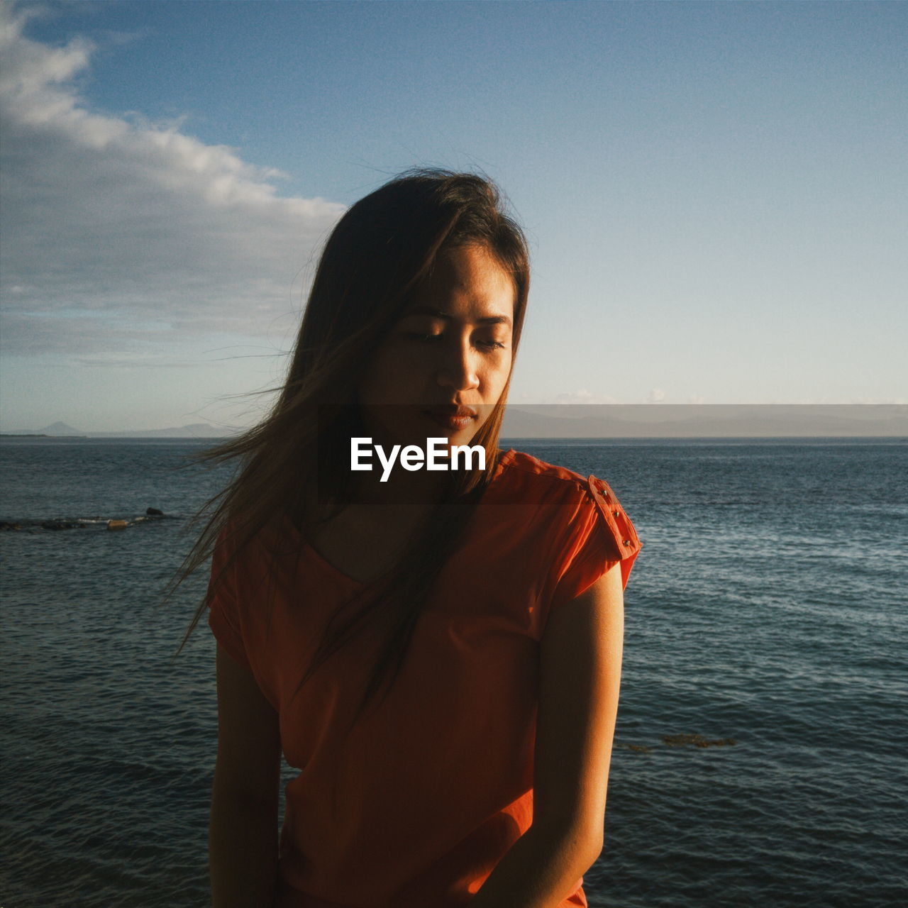 Close-up of woman looking down while sitting by sea against sky