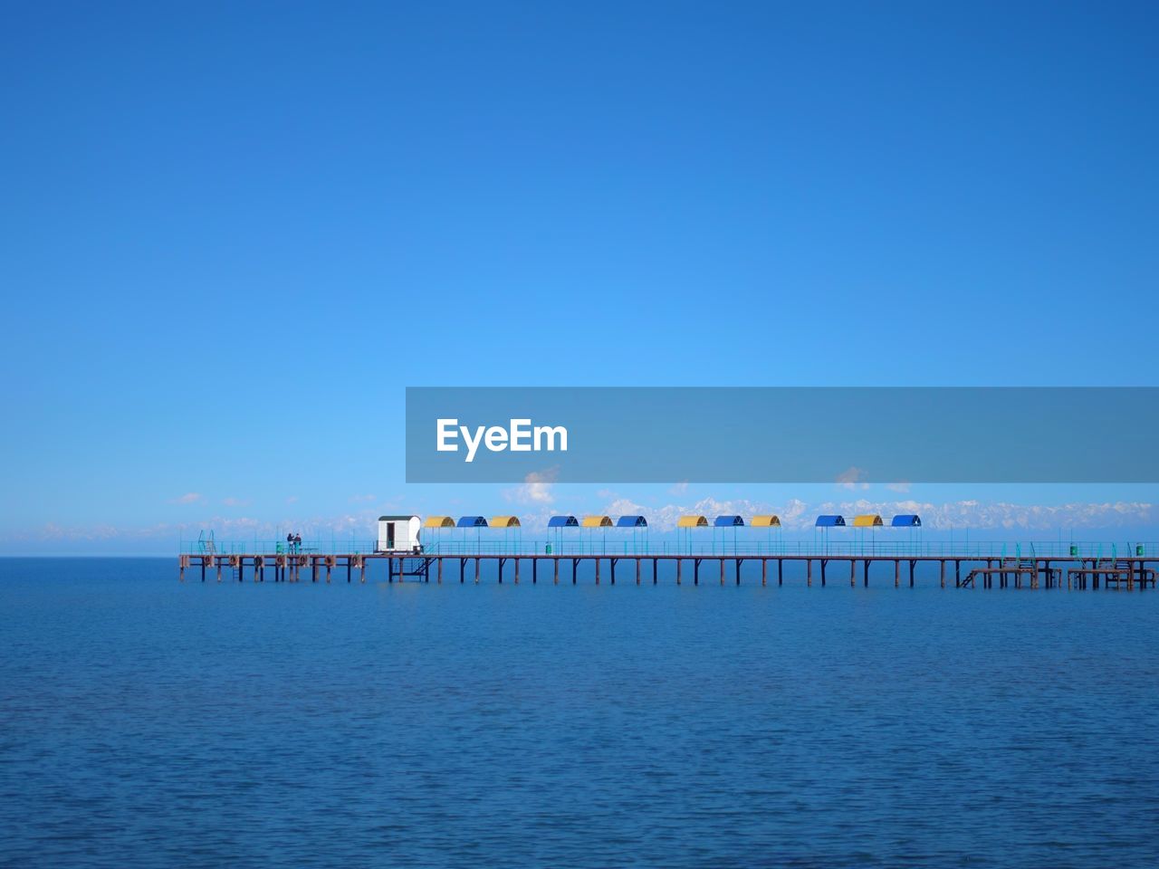 Pier over sea against clear blue sky