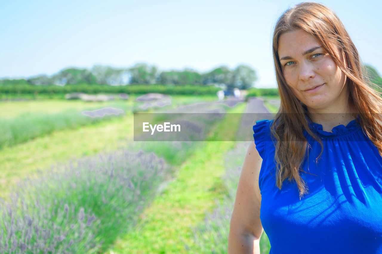 PORTRAIT OF BEAUTIFUL YOUNG WOMAN STANDING ON FIELD