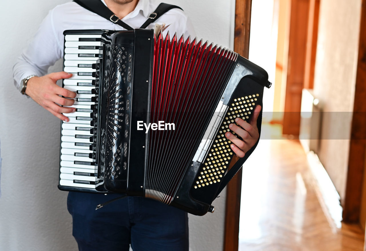 Midsection of man playing accordion at home