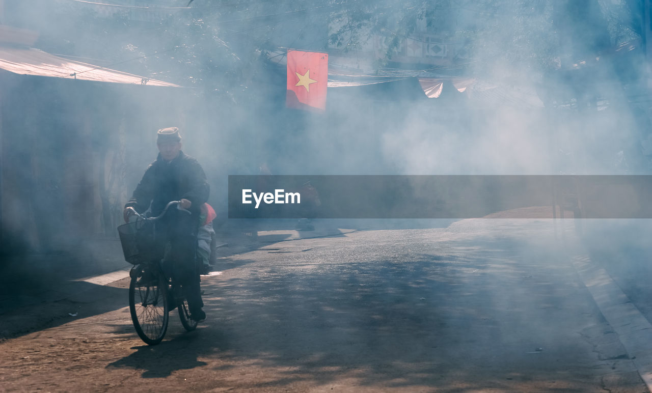 Mature man riding bicycle on road with smoke