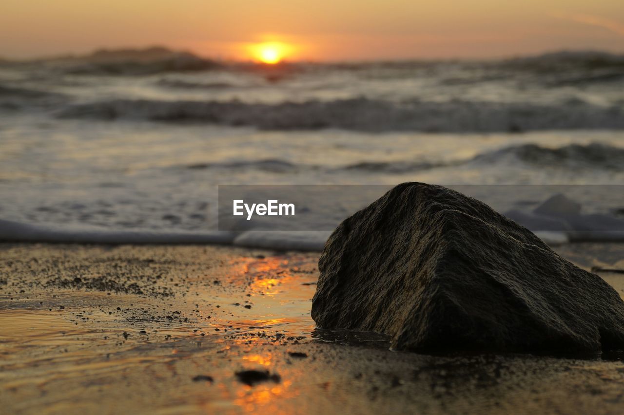 Rock on shore at beach against sky during sunset