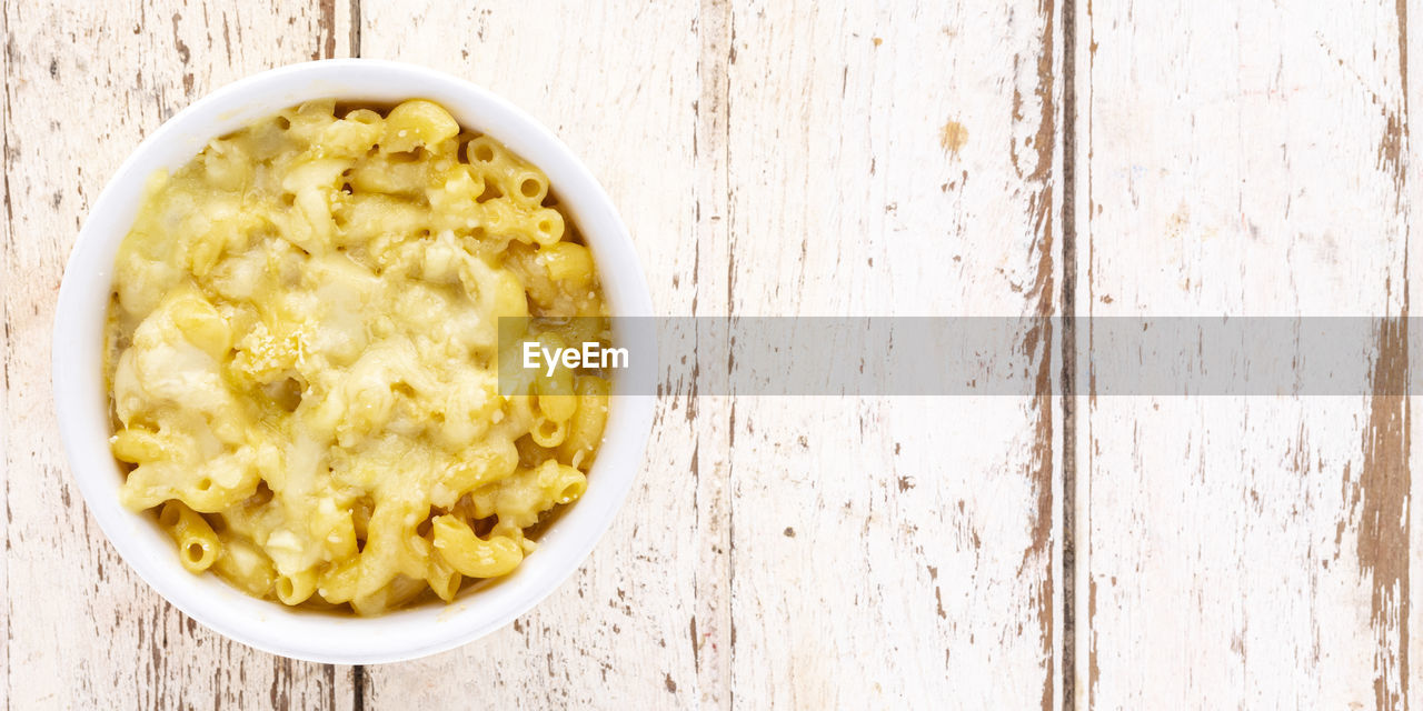 Mac and cheese, macaroni pasta with cheese in ceramic bowl on white old wood texture background, 2x1