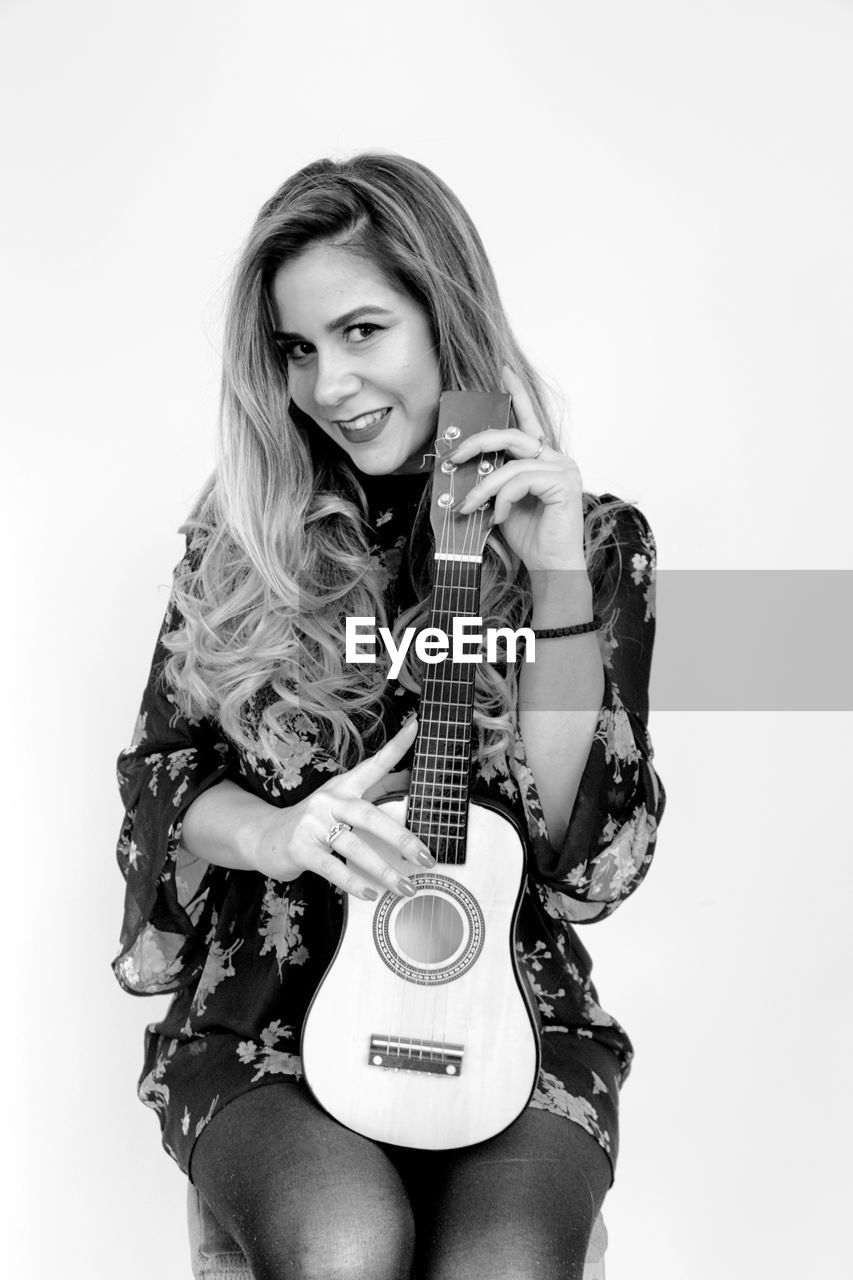 Portrait of beautiful young woman holding ukulele against white background