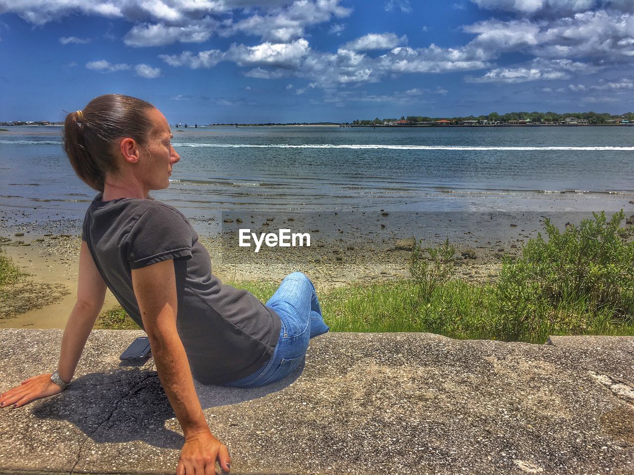 Young woman sitting on retaining wall against sea