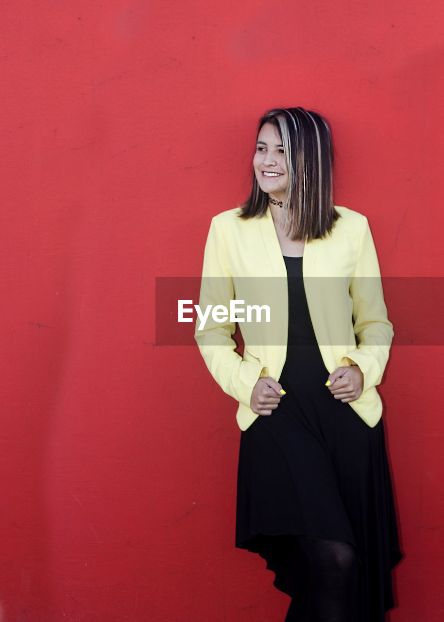 Happy young woman standing against red wall