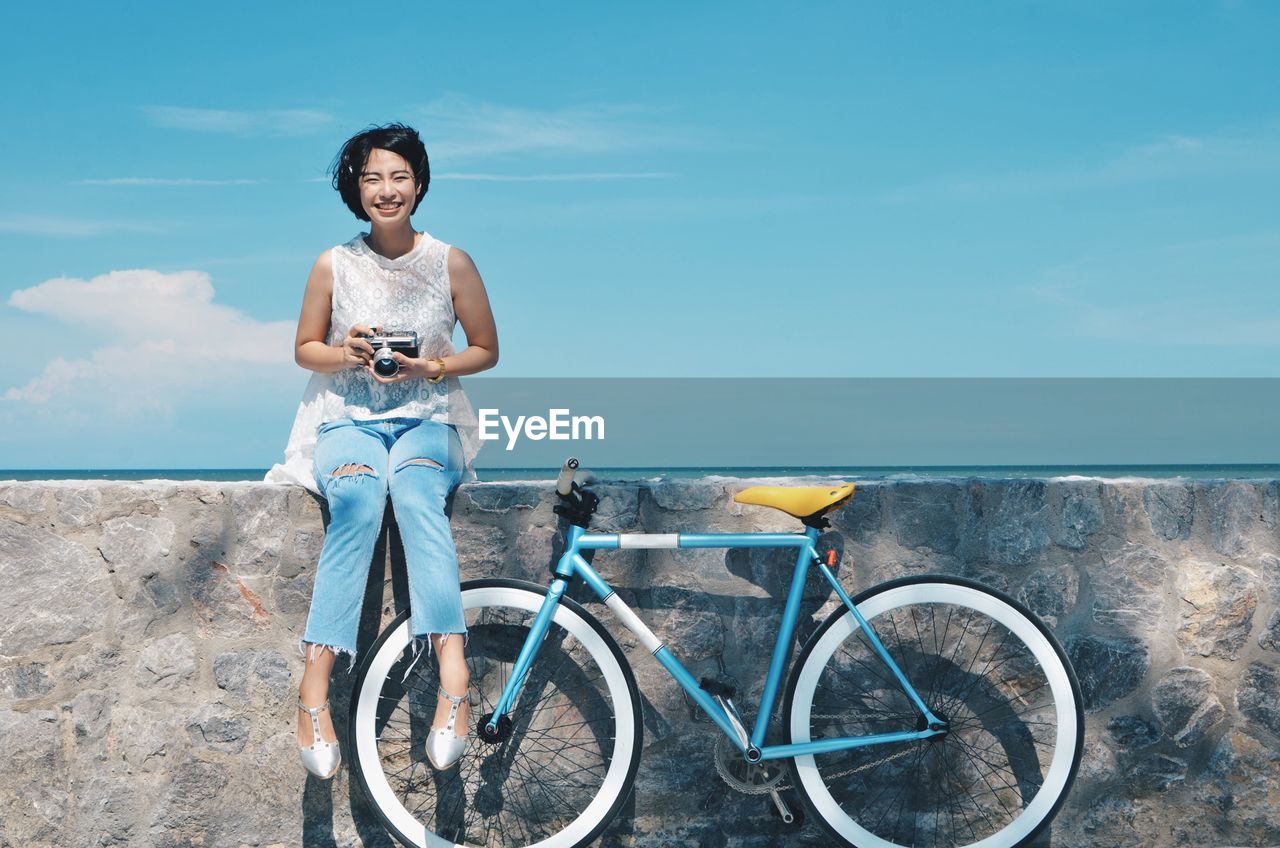 PORTRAIT OF HAPPY YOUNG WOMAN STANDING ON BICYCLE