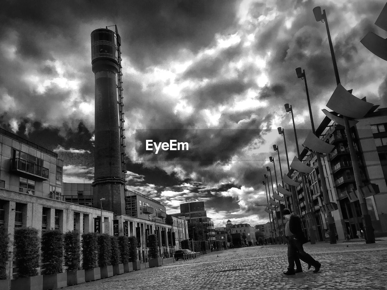 Men walking on street amidst buildings against cloudy sky