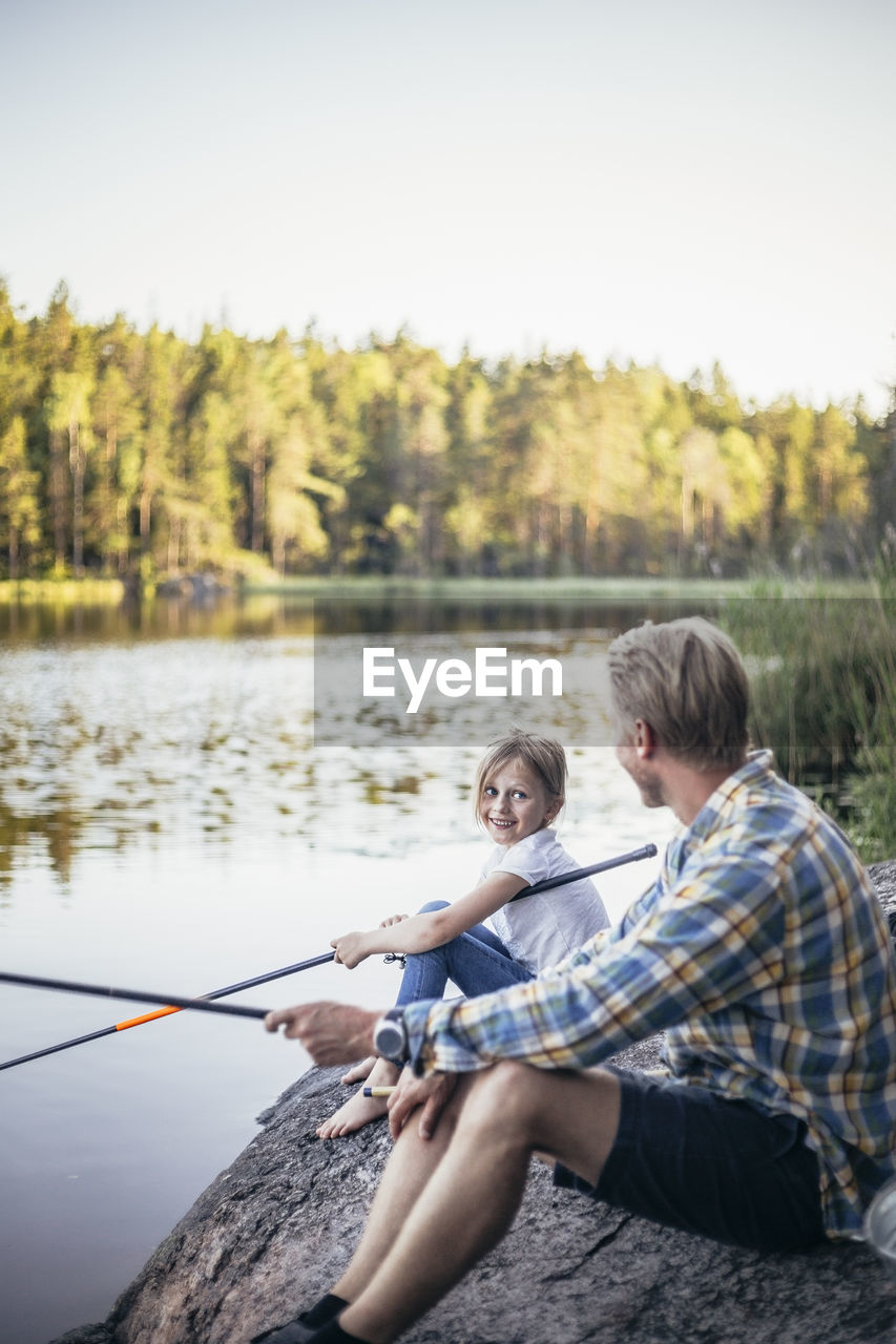 Smiling daughter looking at father while fishing at lake