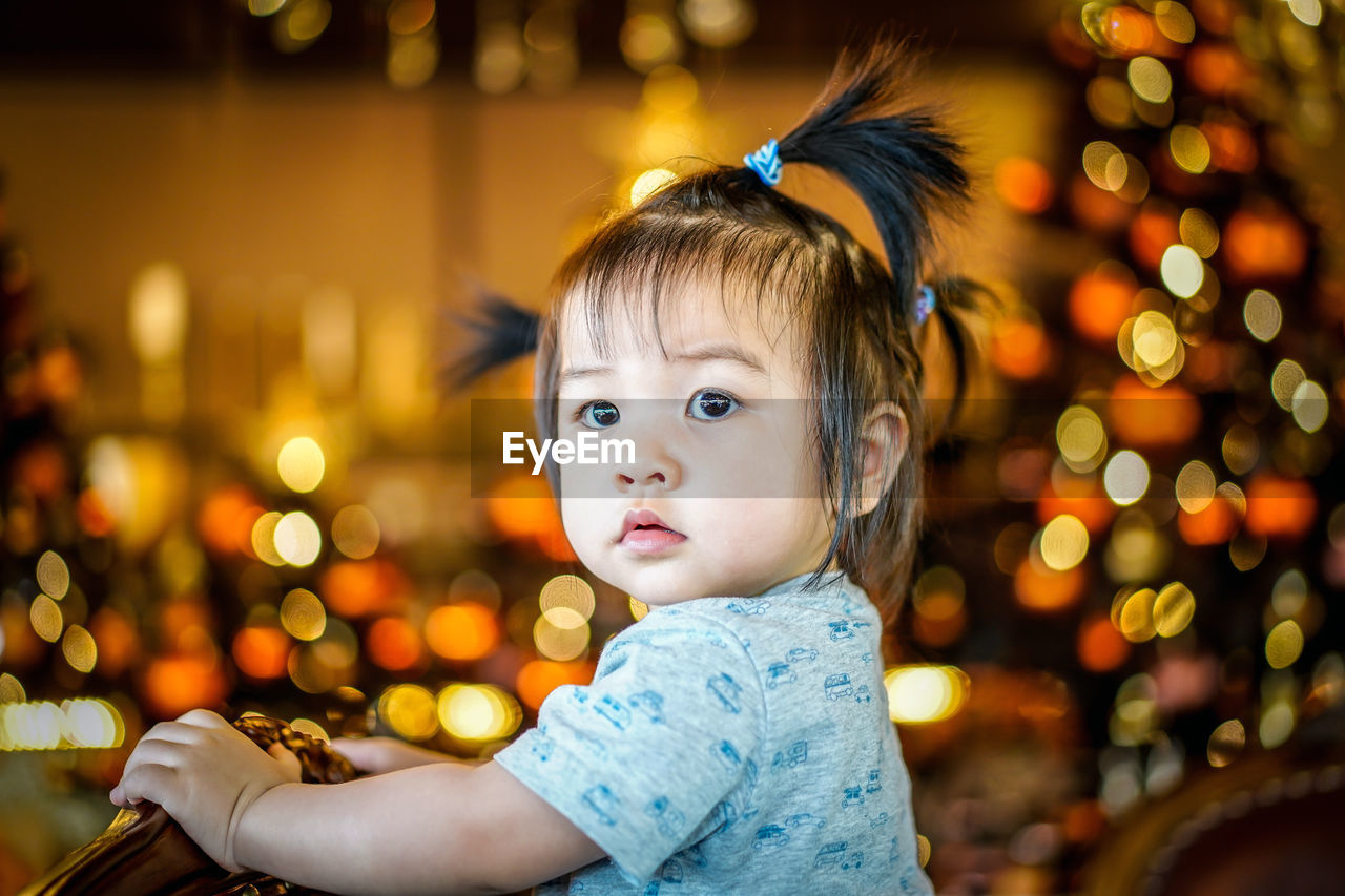 Portrait of cute girl looking away with curly hairstyle on gold bokeh light background. 