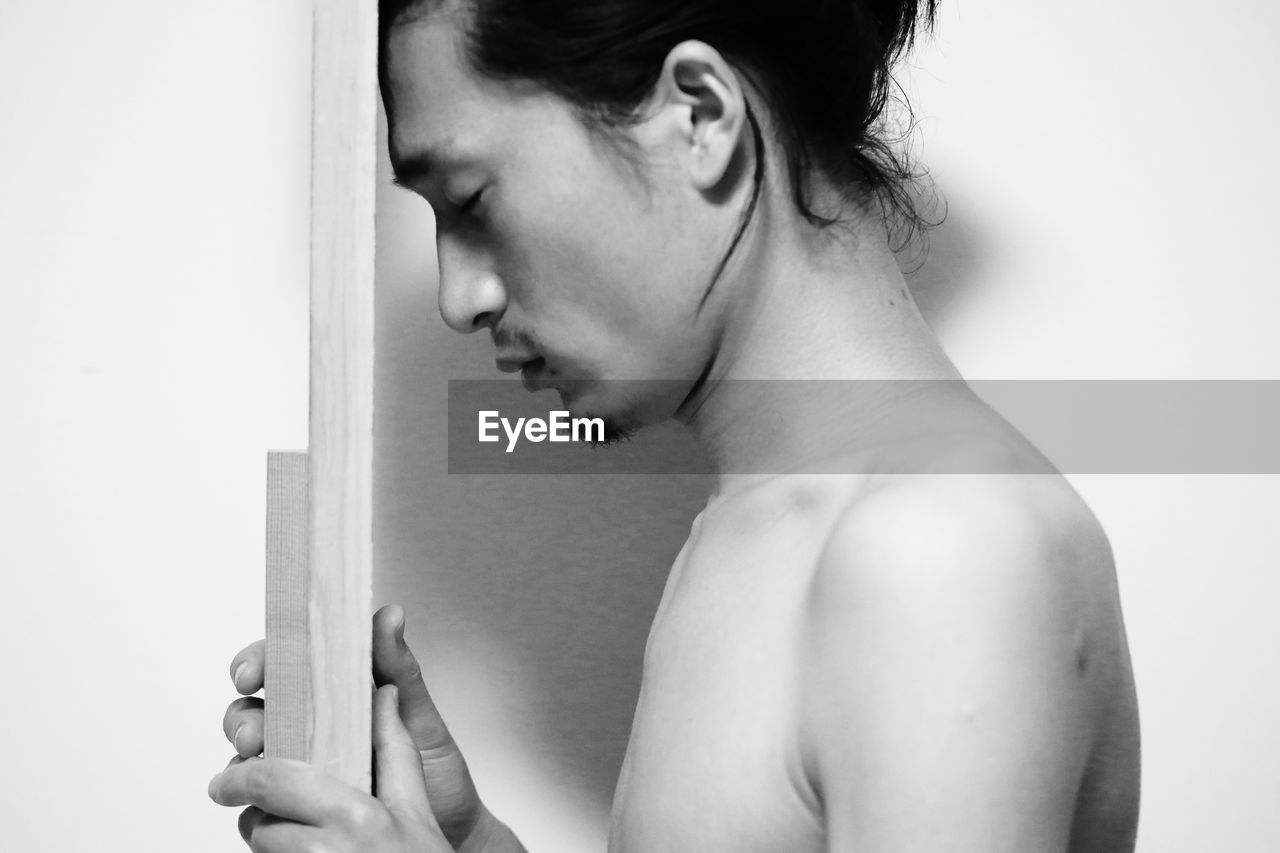 Profile view of shirtless man holding plants by wall