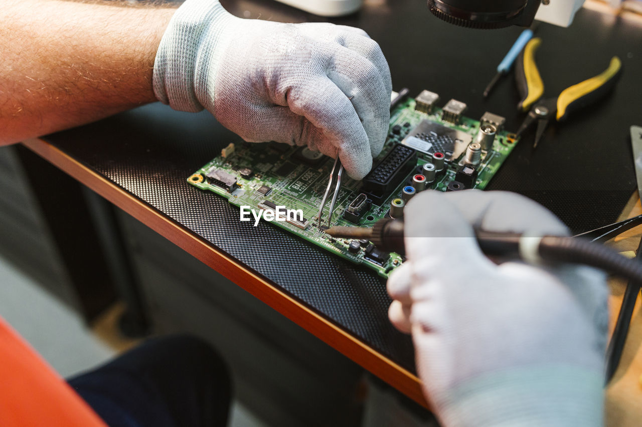 Technician soldering circuit board of electrical component at workbench in electronics repair shop