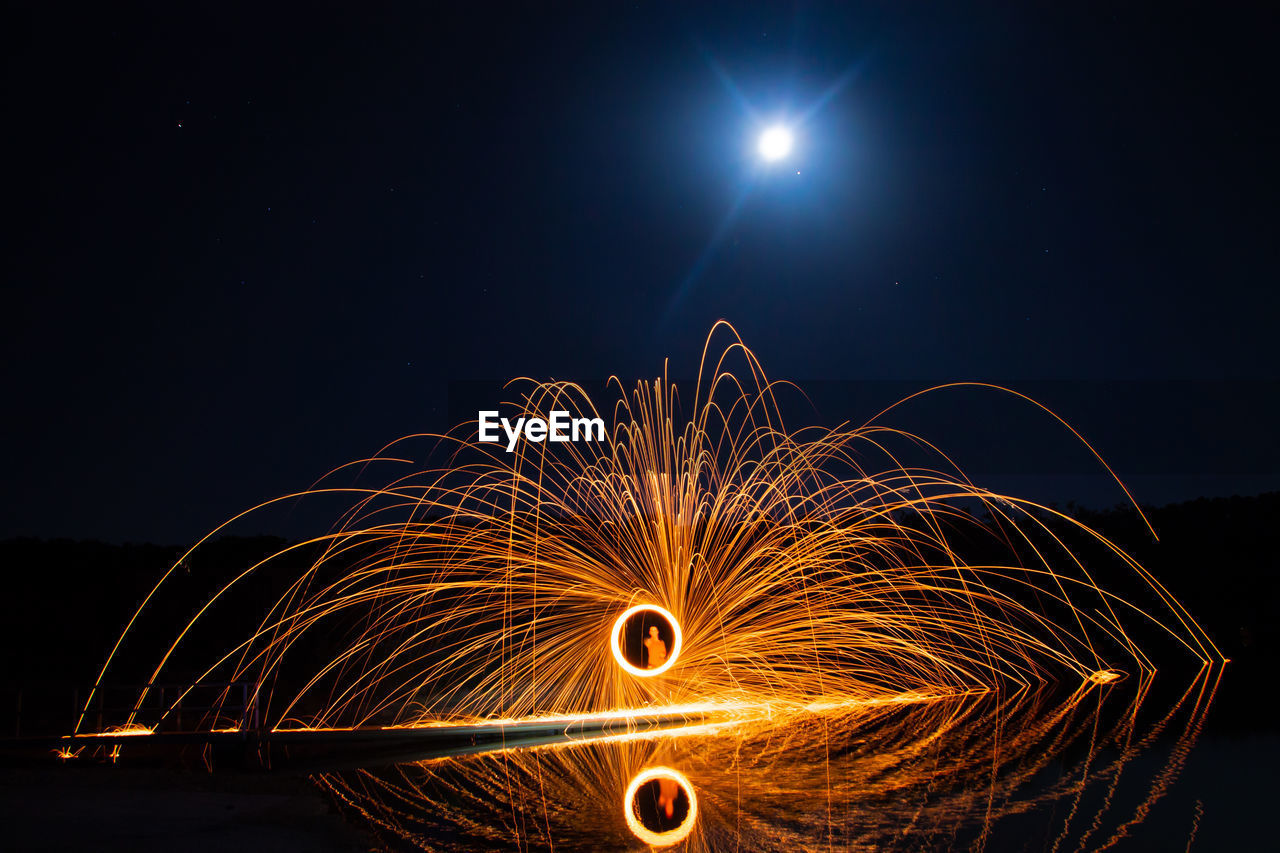 Man spinning wire wool at lakeshore during night