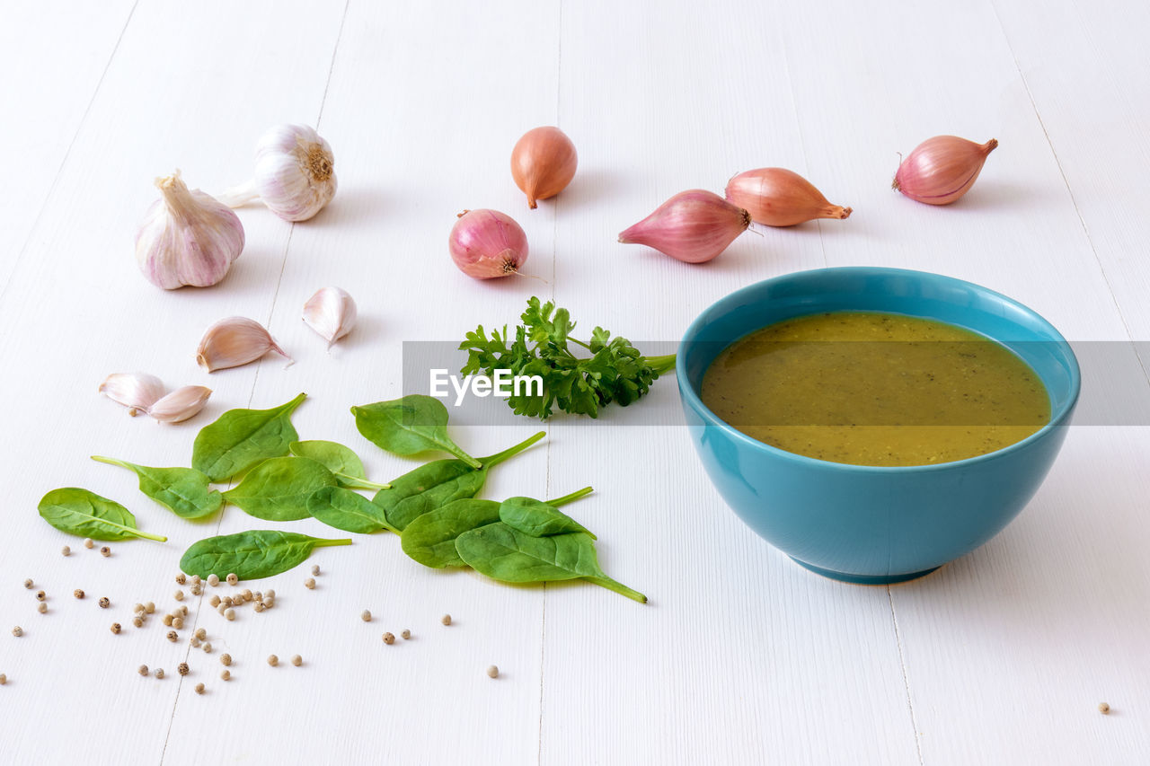 High angle view of a bowl of spinach soup and ingredients on a white table.