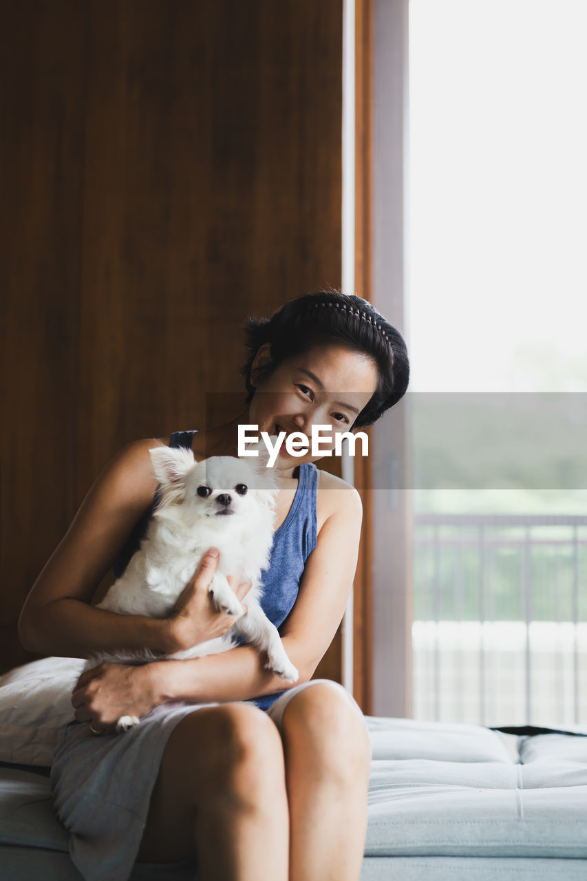 Portrait of cute girl sitting on sofa holding dog at home