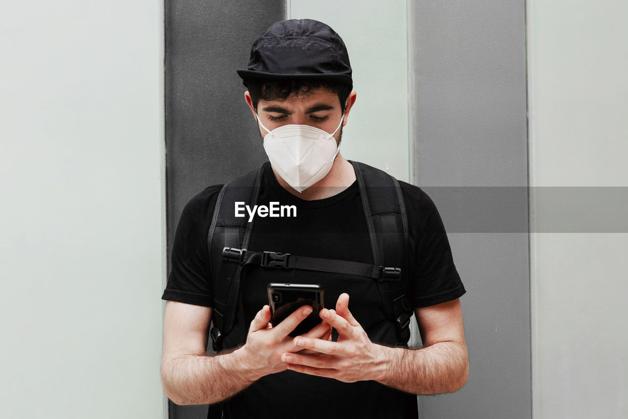 Male in black wear with rucksack using cellphone during quarantine period