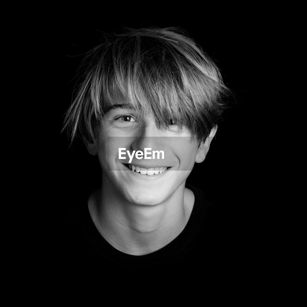 Portrait of smiling teenage boy against black background