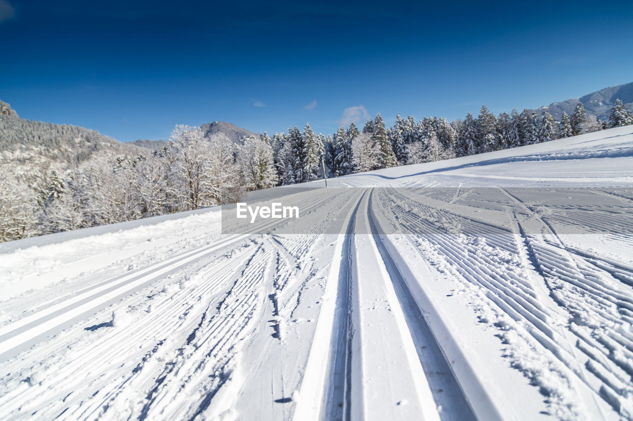 Tire tracks on snow covered land against blue sky