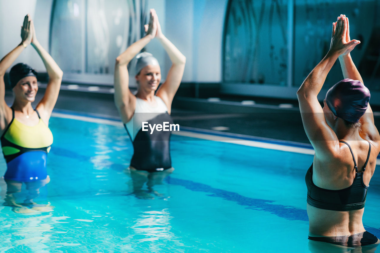 Swimmers with arms raised exercising in swimming pool