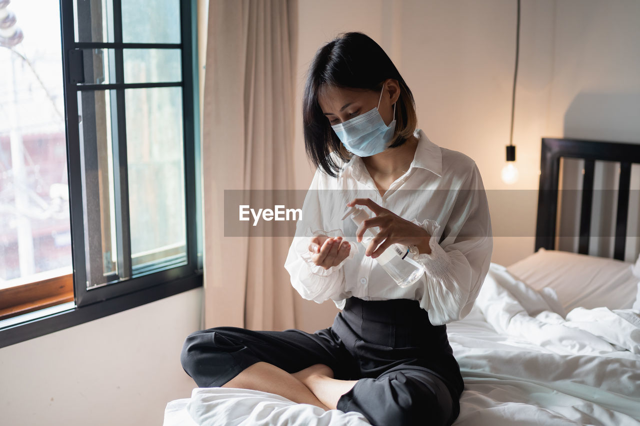 Young woman using hand sanitizer while bed at home