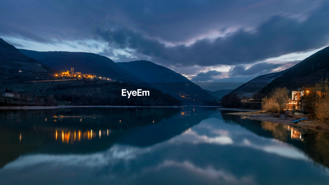 Scenic view of lake by illuminated mountains against sky