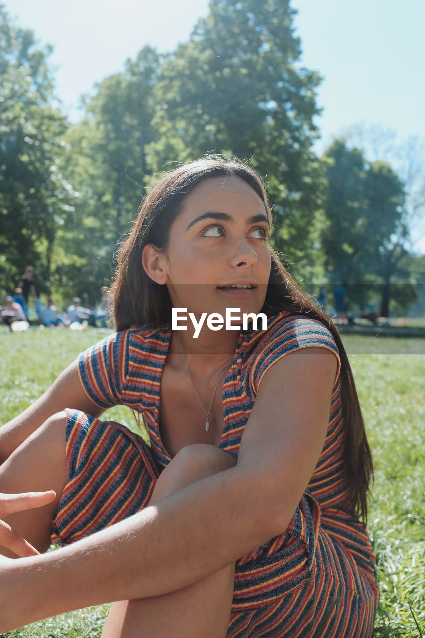 Beautiful young woman looking away while sitting in park