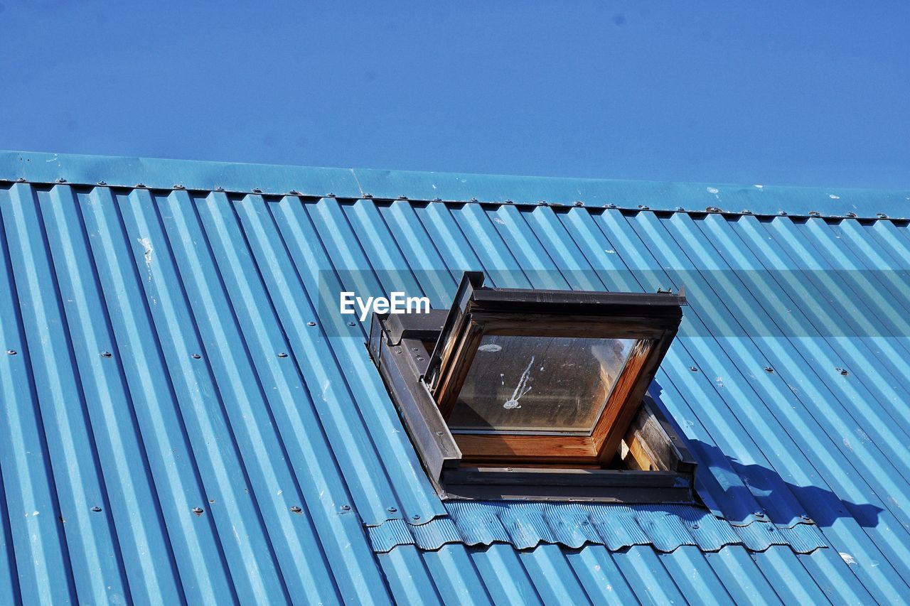 Low angle view of open window on blue metallic roof against clear sky