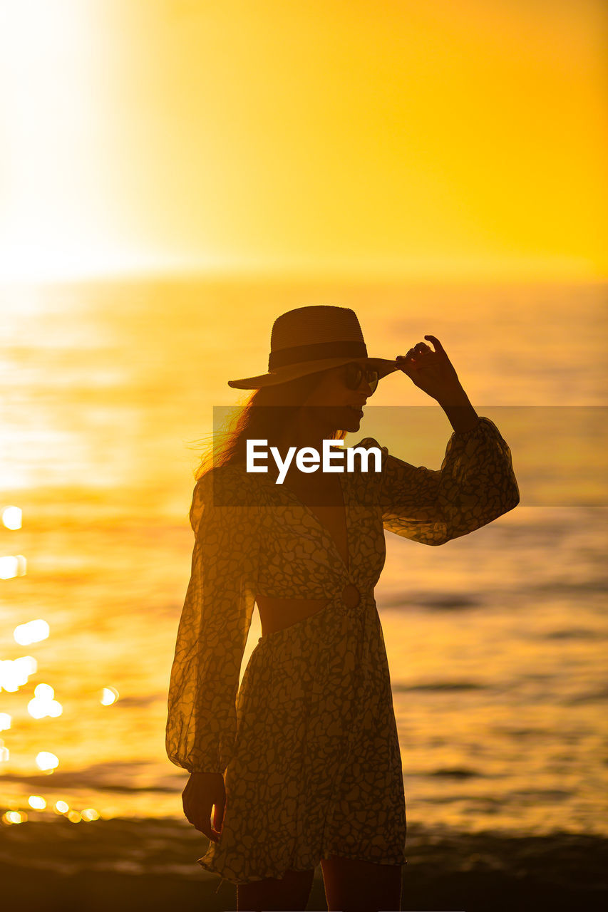 side view of silhouette woman standing at beach during sunset