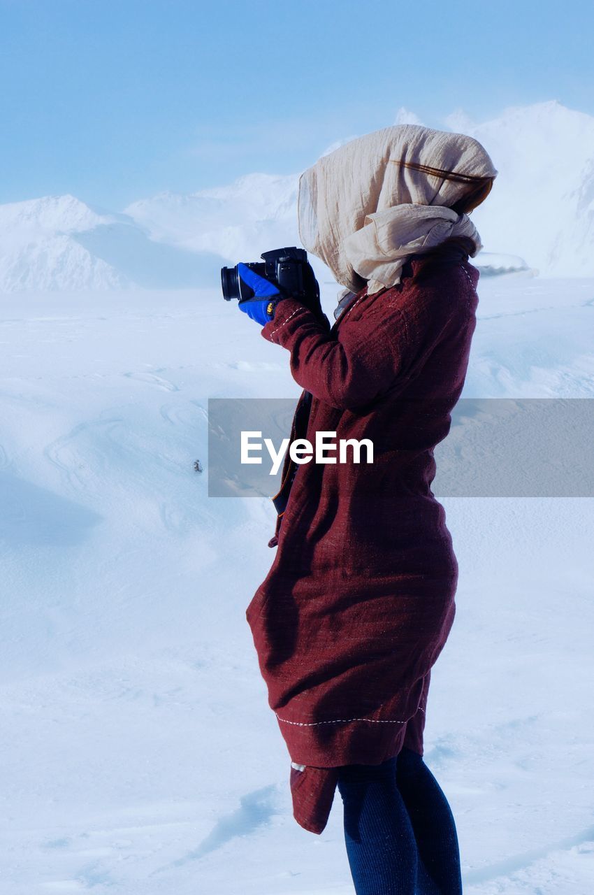 Side view of woman photographing on snowcapped mountain