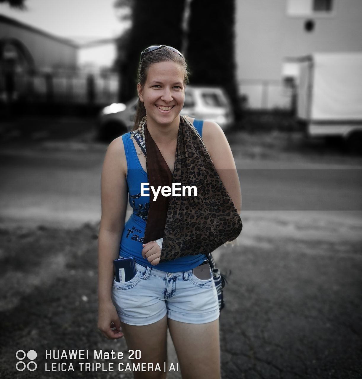 PORTRAIT OF SMILING YOUNG WOMAN STANDING AGAINST BLURRED BACKGROUND